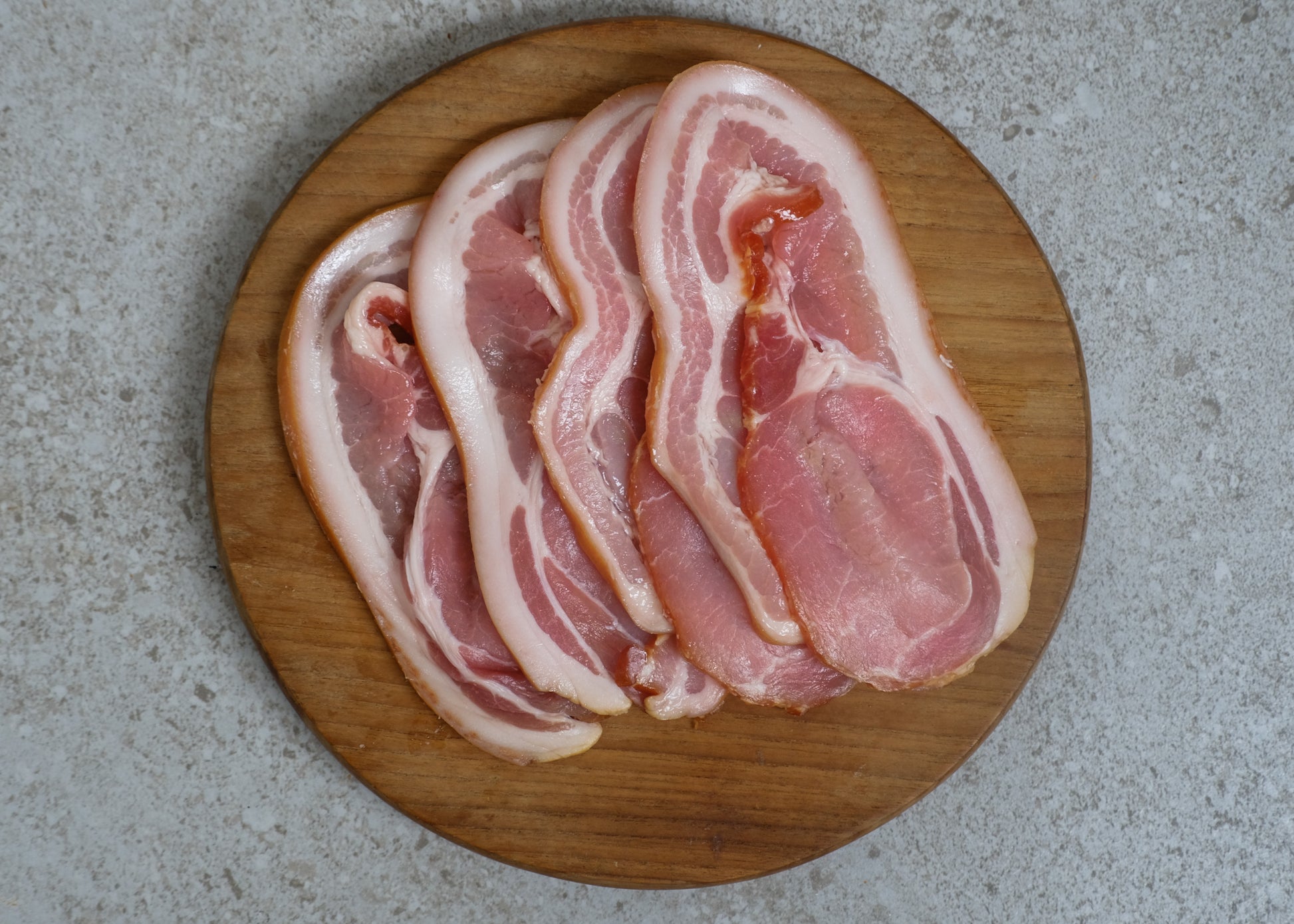 Uncooked bacon slices on a wooden board.